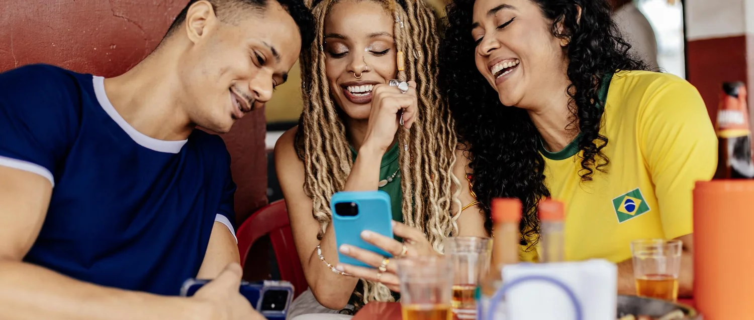 Amigos reunidos à mesa, sorrindo em volta de um celular