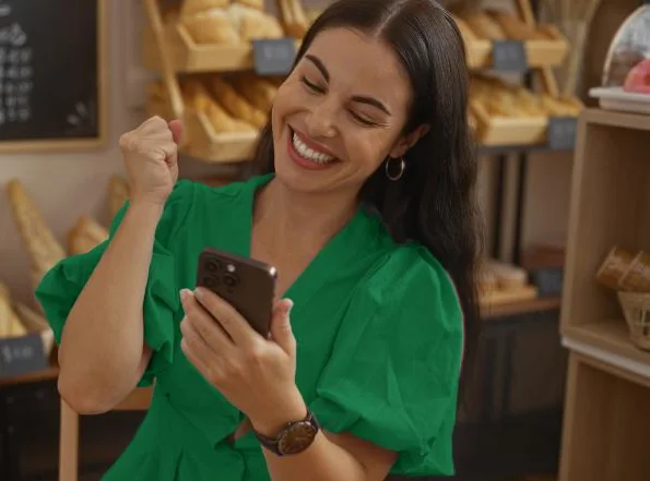 Comerciante sorrindo com o celular na mão, dentro da sua loja
