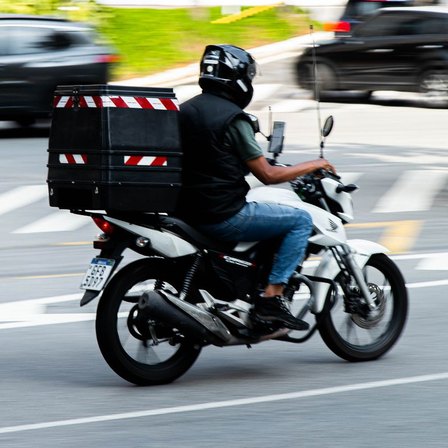 Entregador de moto com bau, no trânsito da região
